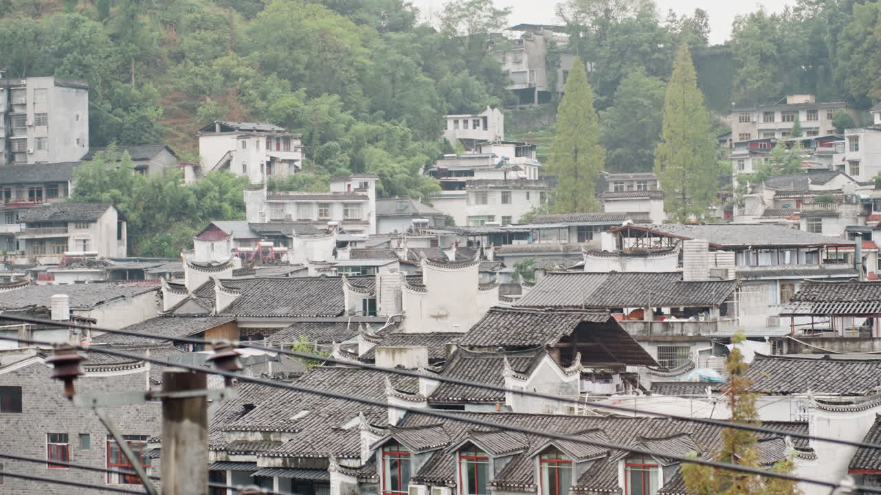 Tetti estesi di hotel in un borgo storico, mattinata nuvolosa con tegole in ceramica sovrapposte, comignoli, vicoli stretti e una collina verde in lontananza, atmosfera tranquilla che suggerisce un'ispezione alberghiera.