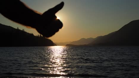 sunset on a lake with mountains in the background with a guy giving the thumbs up in silhouette