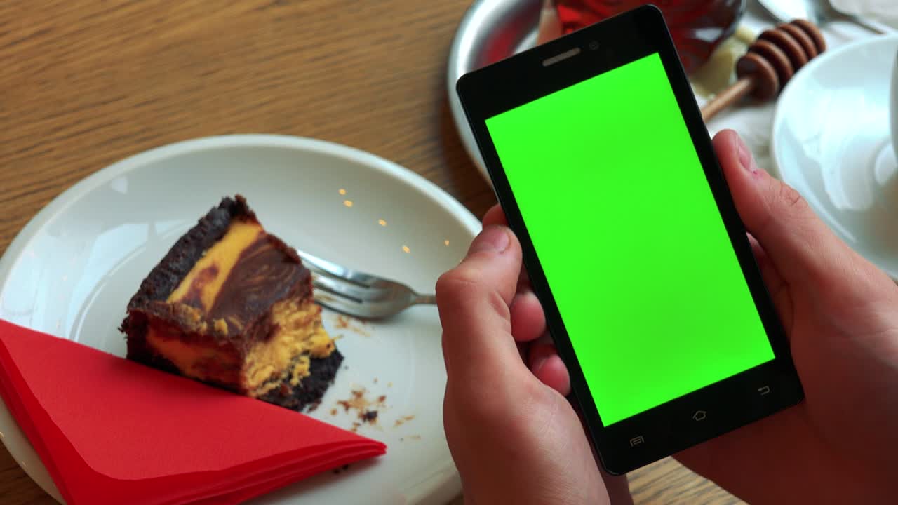 un hombre sostiene un teléfono inteligente con una pantalla verde sobre una mesa con comida - primer plano desde arriba en el teléfono inteligente