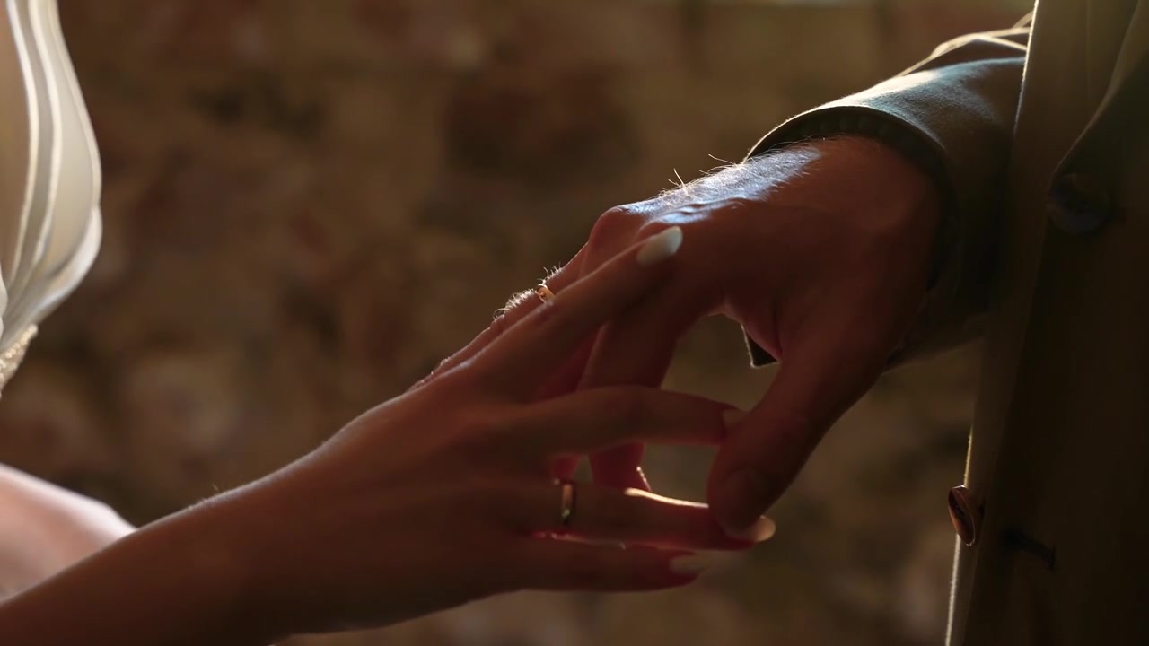 Close-up shot of a bride and groom tenderly exchanging wedding rings in soft natural light, highlighting emotion, delicate hands, elegant attire, and the intimacy of the moment.