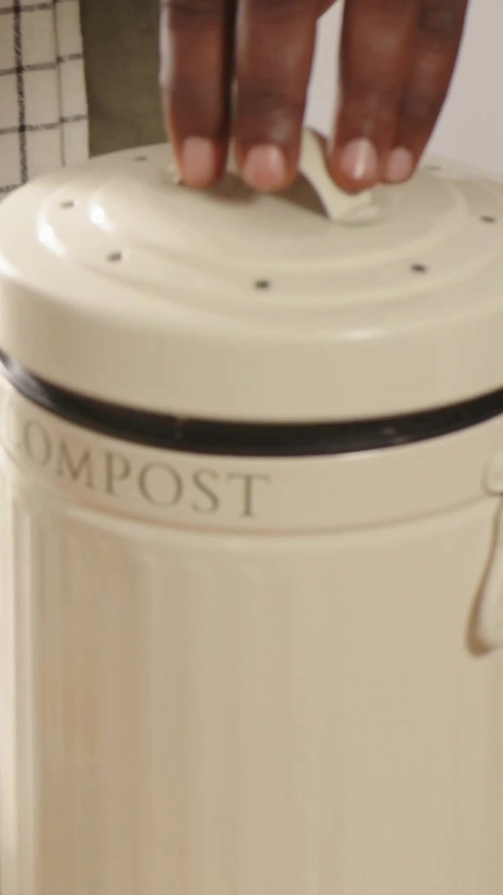 Vidéo verticale: Main à manche verte soulevant le couvercle, vérifiant le bac à compost sur le comptoir, révélant la doublure