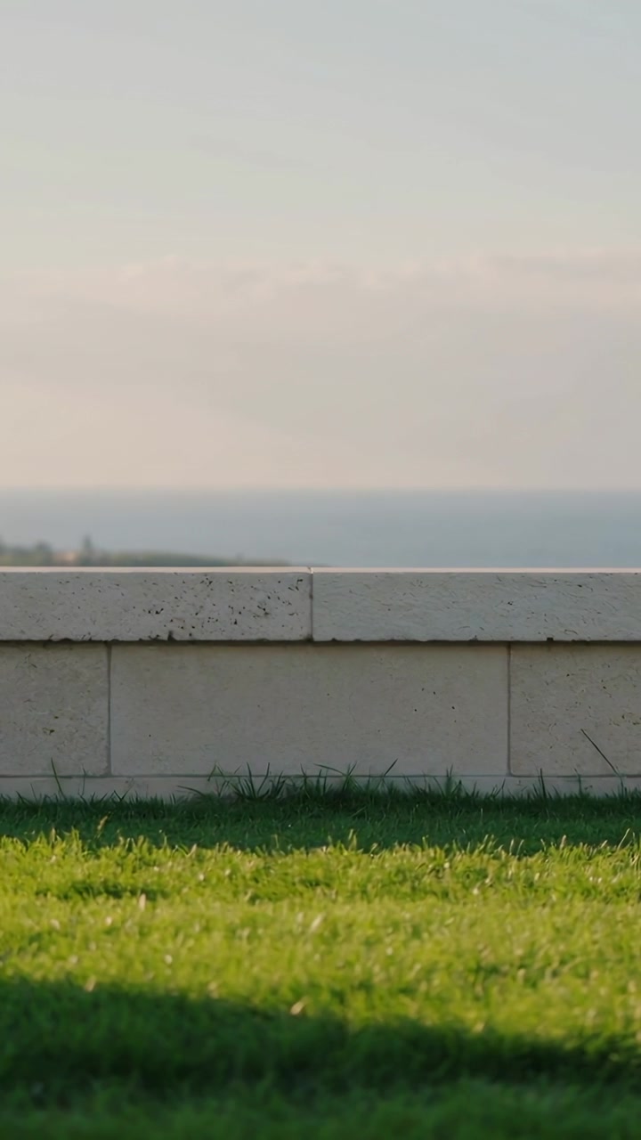 Video verticale: Ripresa di un muro di pietra e di erba curata in riva al mare, con la brezza che sposta le nuvole.