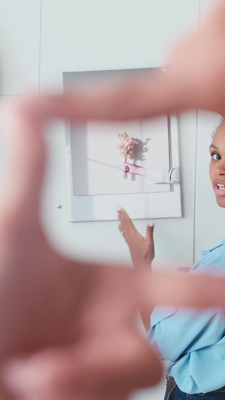 Young attractive african american business woman hangs picture on wall in office
