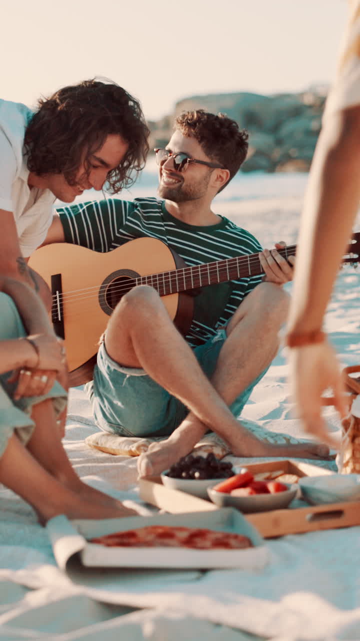 Giovane uomo che suona la chitarra per gli amici a un picnic in spiaggia.