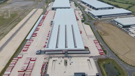 drone aerial cinematic view of large logistics warehouse hub with trucks loading and unloading trailers at distribution centre lutterworth england united kingdom