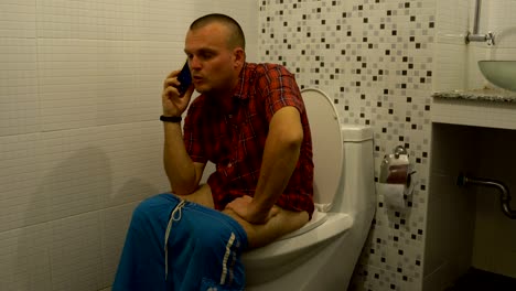 a man sits on a toilet and talking on the phone