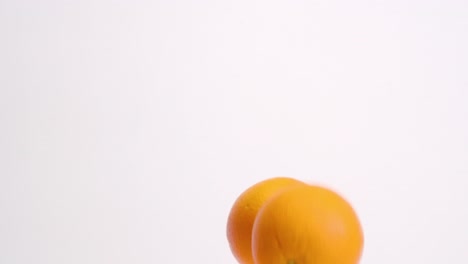 whole oranges falling on white studio backdrop in 4k slow motion