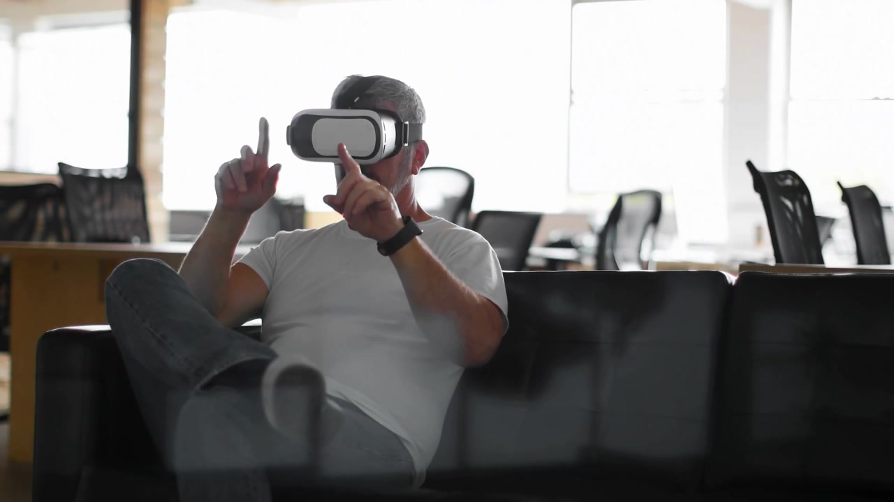Tecnico seduto sul divano con visore VR che testa l'interfaccia VR su particelle rosse che appaiono e svaniscono.