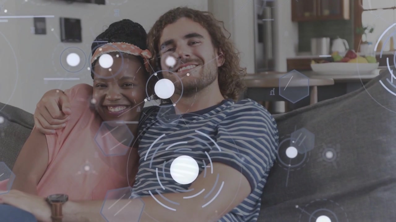 Coppia appoggiata sul divano, overlay tecnologico che attraversa la telecamera rivelando sorrisi e condividendo affetto.