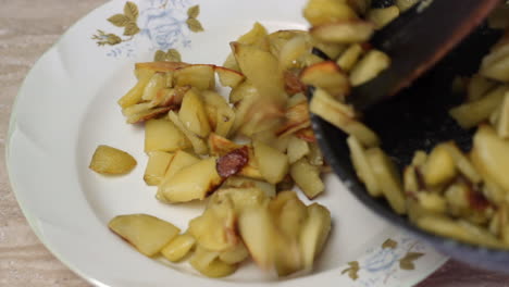 Cooked-potatoes-served-into-white-plate-with-wooden-spatula,-close-up