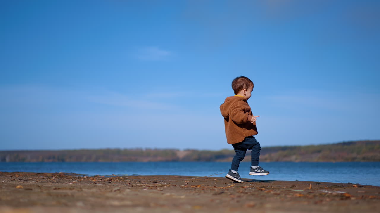 Toddler boy picks a stone and goes to water. Energetic kid throws the stone into river. Low angle view.