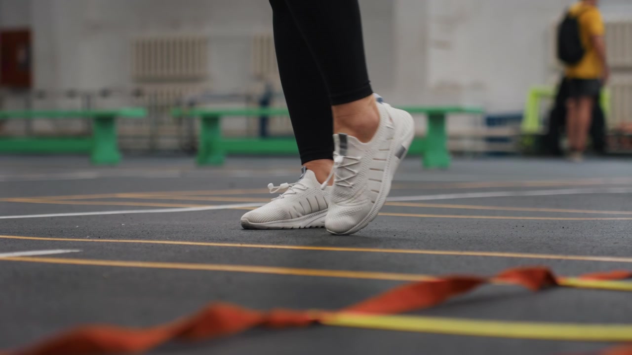 L'istruttore guida esercizi di agilità rapidi utilizzando nastri da palestra e segnaletica del campo. I partecipanti si impegnano in esercizi di agilità specifici per il badminton con movimenti rapidi e un allenamento preciso del gioco di gambe.