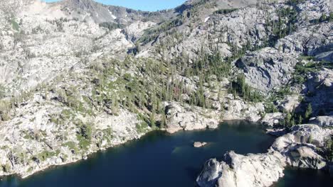 Eine-Langsam-Stabilisierte-4K-Drohnenluftaufnahme-Zeigt-Einen-Alpensee-Am-Fuße-Einer-Bergkette-In-Der-Wildnis-In-Der-Nähe-Von-Lake-Tahoe-Mit-Schnee-Und-Bäumen-Beim-Camping-Und-Rucksackwandern-In-Der-Nähe-Von-Lake-Tahoe