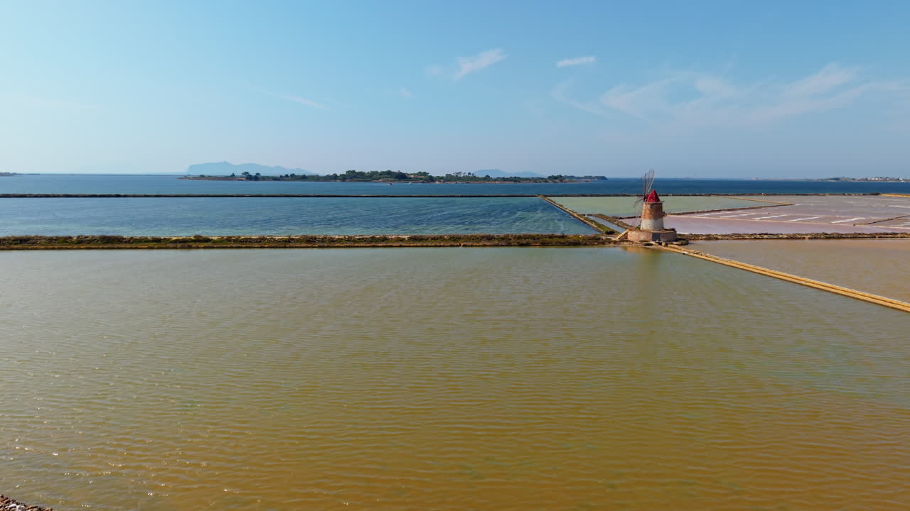 Stunning drone view of colorful salt pans with traditional windmill in Sicily, Italy, bright water pools, blue sea and clear sky