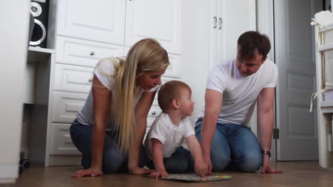 a family of three in white t-shirts and blue jeans sitting on the floor of their bedroom playing with the boy in intellectual games. slow-motion shooting happy family