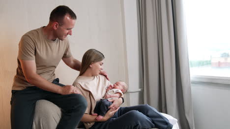 woman with a child sits on the sofa. husband sits on the sofa back looking at baby and caressing his wife.