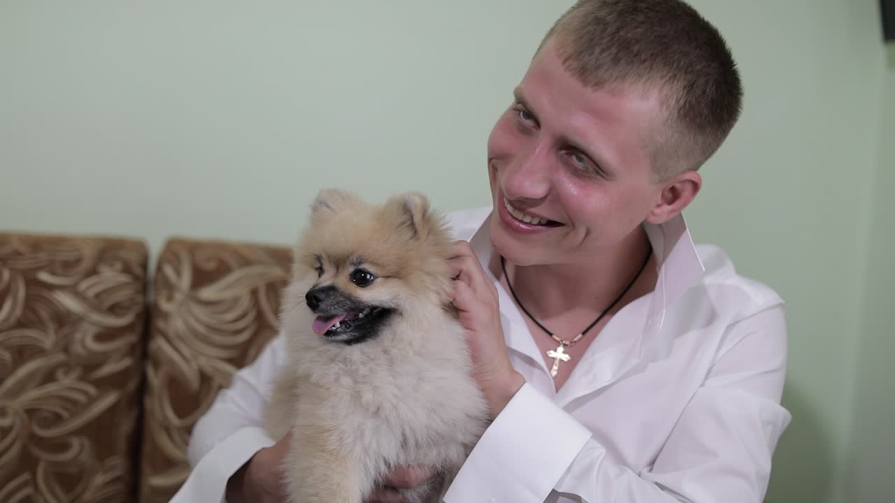 한 남자가 소파에서 개를 키우며 미소 짓는다