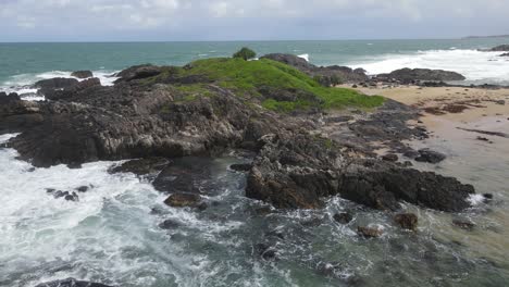 playa de sawtell - isla rocosa cubierta de plantas verdes y golpeada por olas rompientes en sawtell, nsw, australia