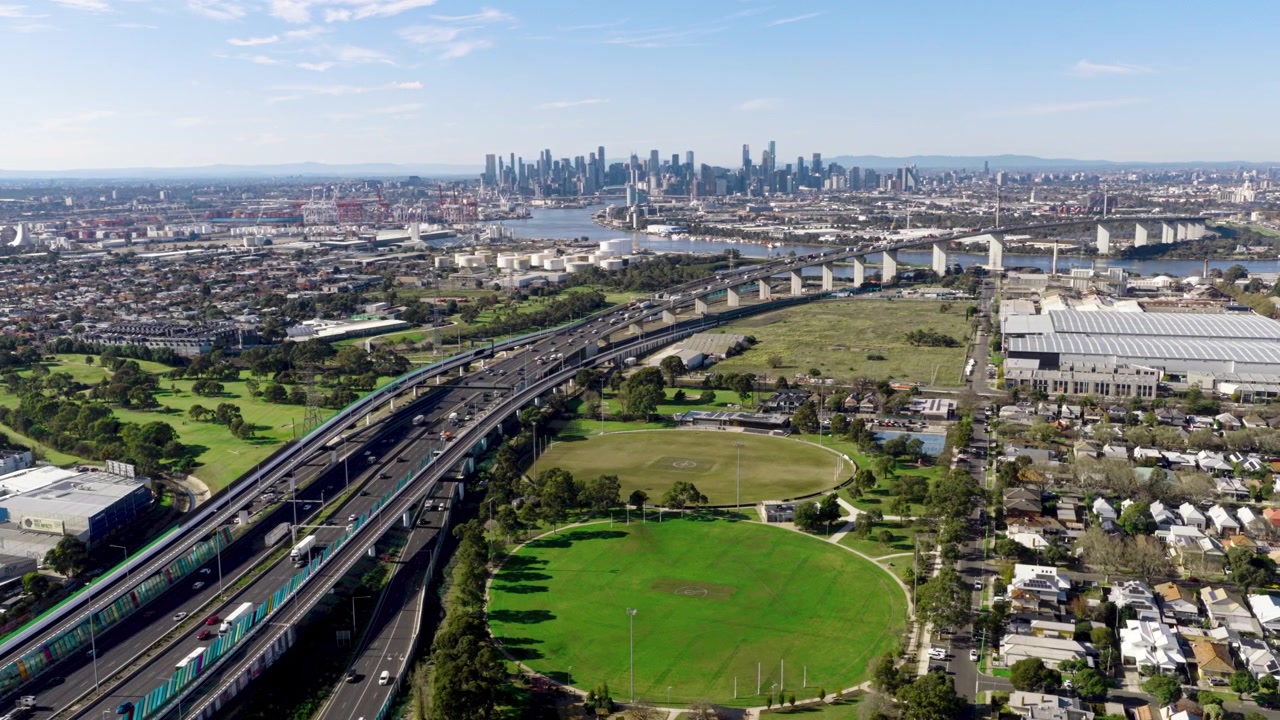 Široký letecký pohled na panorama centrální obchodní čtvrti Melbourne, dálnici West Gate Freeway, přístav Melbourne a okolní parky, představující městskou dopravní síť a ikonickou městskou krajinu