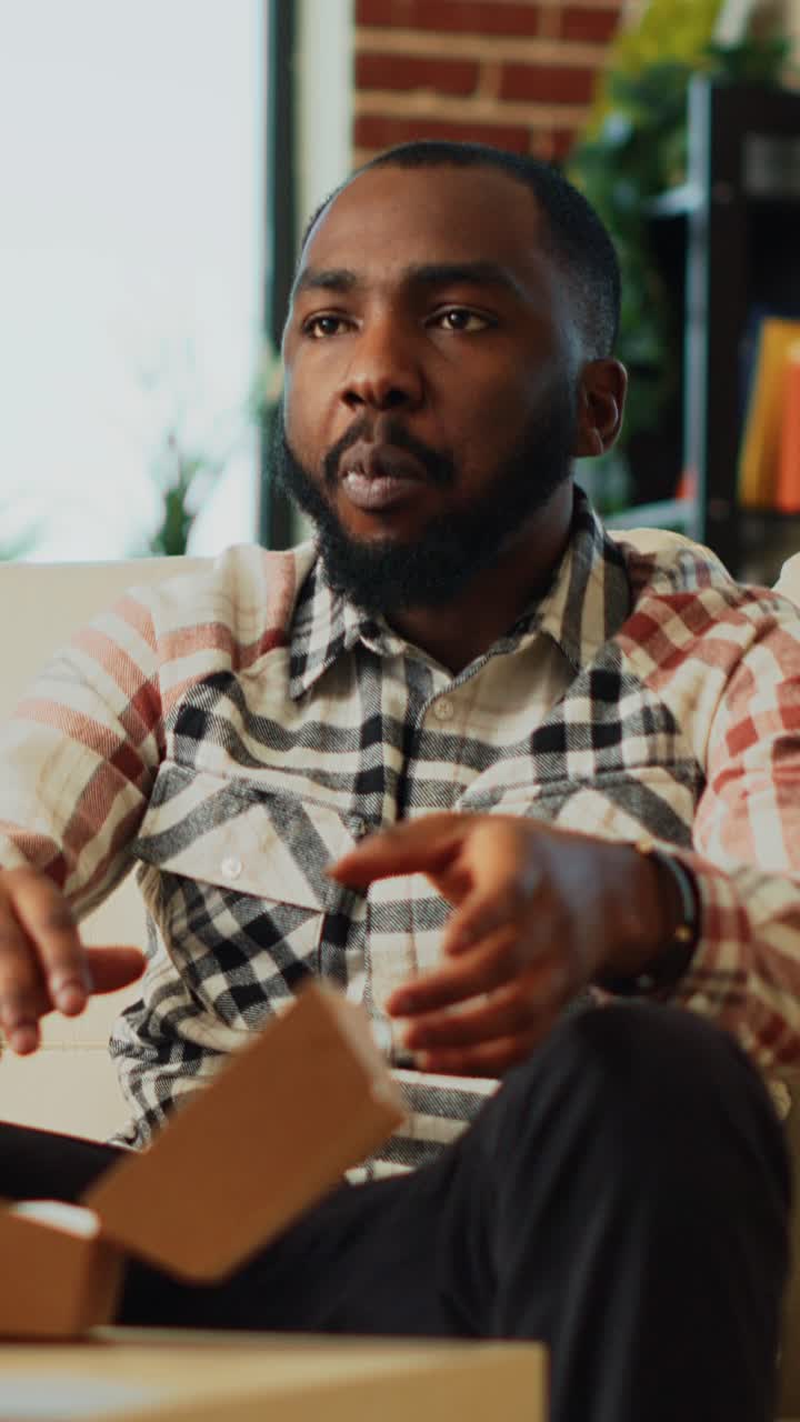 Vertical video: African american man taking bite of hamburger with fries
