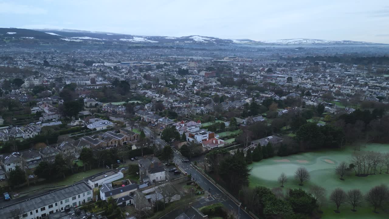 Dolly reverse aerial view of Churchtown neighborhood in South dublin, Milltown Gold club and Dublin Mountains in the background during winter time.
