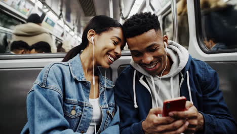 young couple sharing earphones and a smartphone on a subway