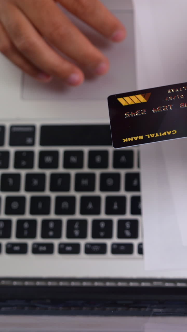 Engaging vertical video showing a hand using a credit card over a laptop keyboard, capturing the essence of online shopping. Bright lighting enhances the tech-driven atmosphere