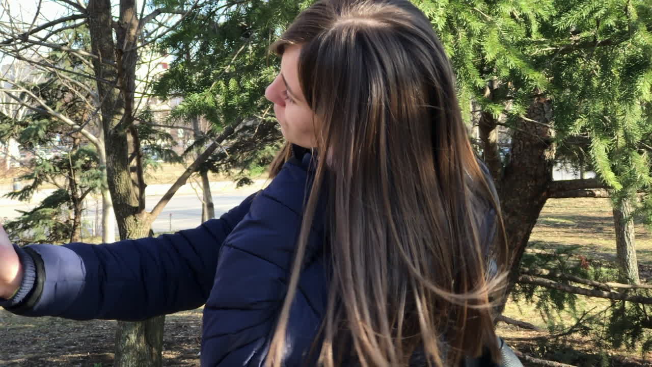 cámara lenta de una joven que se toma selfies con un smartphone usando una cámara frontal en un parque de la ciudad
