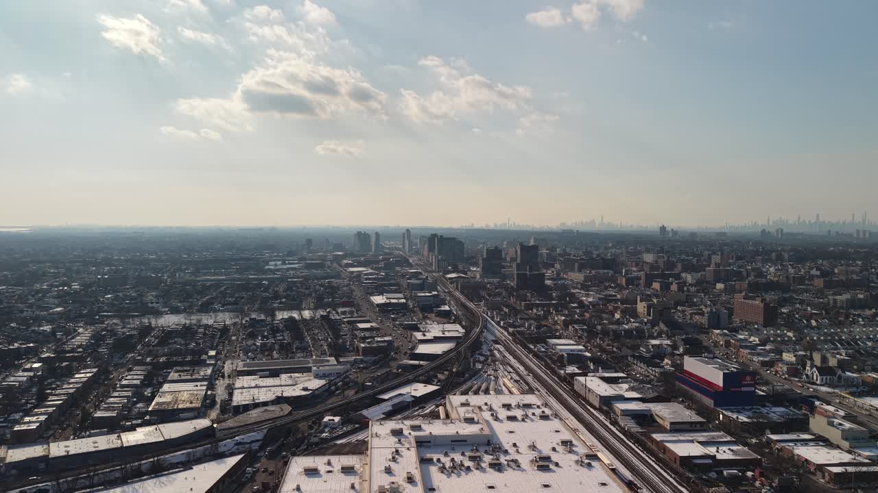 Prospettiva aerea dall'alto che vola all'indietro sopra i tetti innevati di Jamaica, Queens, New York, rivelando i binari della Long Island Rail Road e lo skyline distante di Manhattan