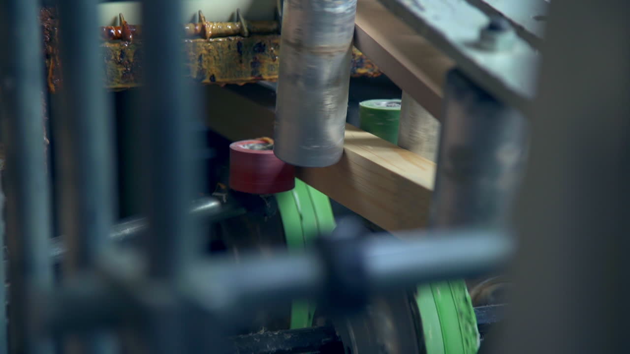 Timber bar in the automated machine. Rollers are rotating sending wooden block along conveyor belt. Close up.