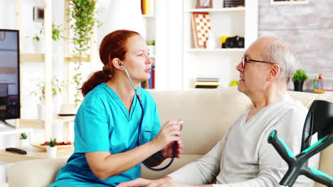 caucasian female nurse listening to elderly retired man heartbeat in bright and cozy nursing home