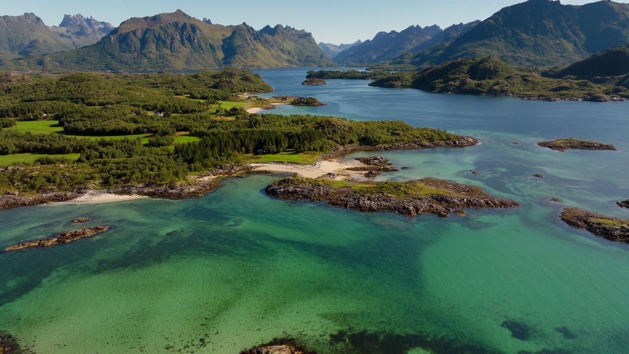 Aerial footage of the clear turquoise waters, beaches, and rugged coastline of Brottøya in the Lofoten Islands, Hadsel Municipality, Norway, captured on a bright summer day