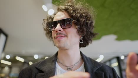 a confident and cool brunette guy with curly hair and wearing black sunglasses walks through the supermarket and looking around the shelves chooses the products he needs