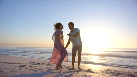 Ein-Gemischtrassiges-Paar-Genießt-Einen-Spielerischen-Spaziergang-Am-Strand-Bei-Sonnenuntergang