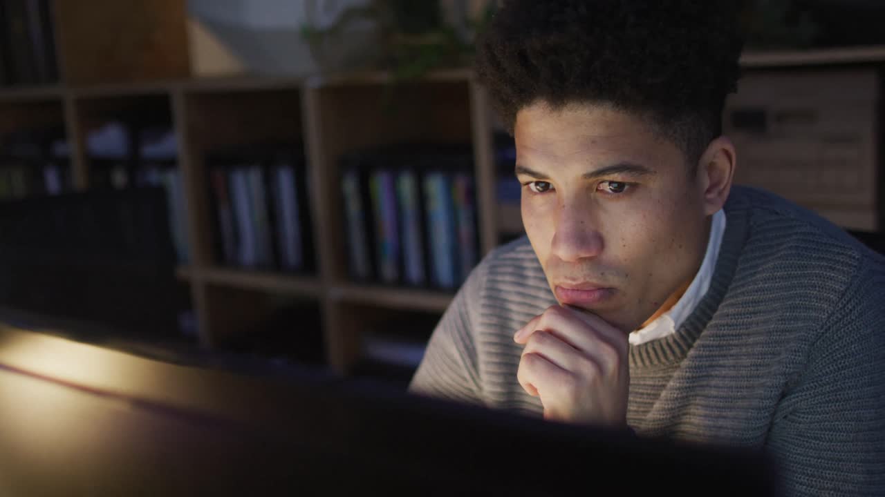 Video of focused biracial man using computer, working late in office