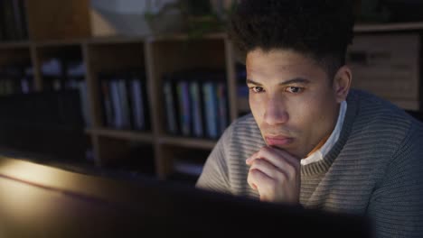 Video-of-focused-biracial-man-using-computer,-working-late-in-office