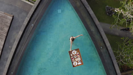 aerial view woman having breakfast in swimming pool enjoying exotic food at luxury hotel spa with view of tropical jungle