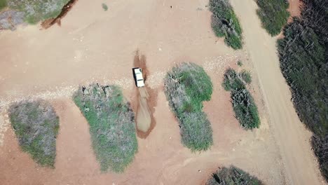 A-white-car-driving-through-a-mud-puddle-in-the-east-of-the-island-of-Bonaire,-Dutch-Caribbean