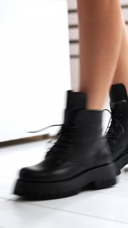 girl with bare legs and black boots starts to jump. model demonstrating the stylish leather footwear with laces at white backdrop. close up. vertical video