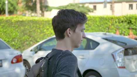 a young male student with a backpack for school walks through a parking lot