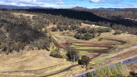 aerial footage captures a winding dirt motorbike track set in dry bushland, with clear skies and natural lighting, showcasing the course layout and surrounding environment