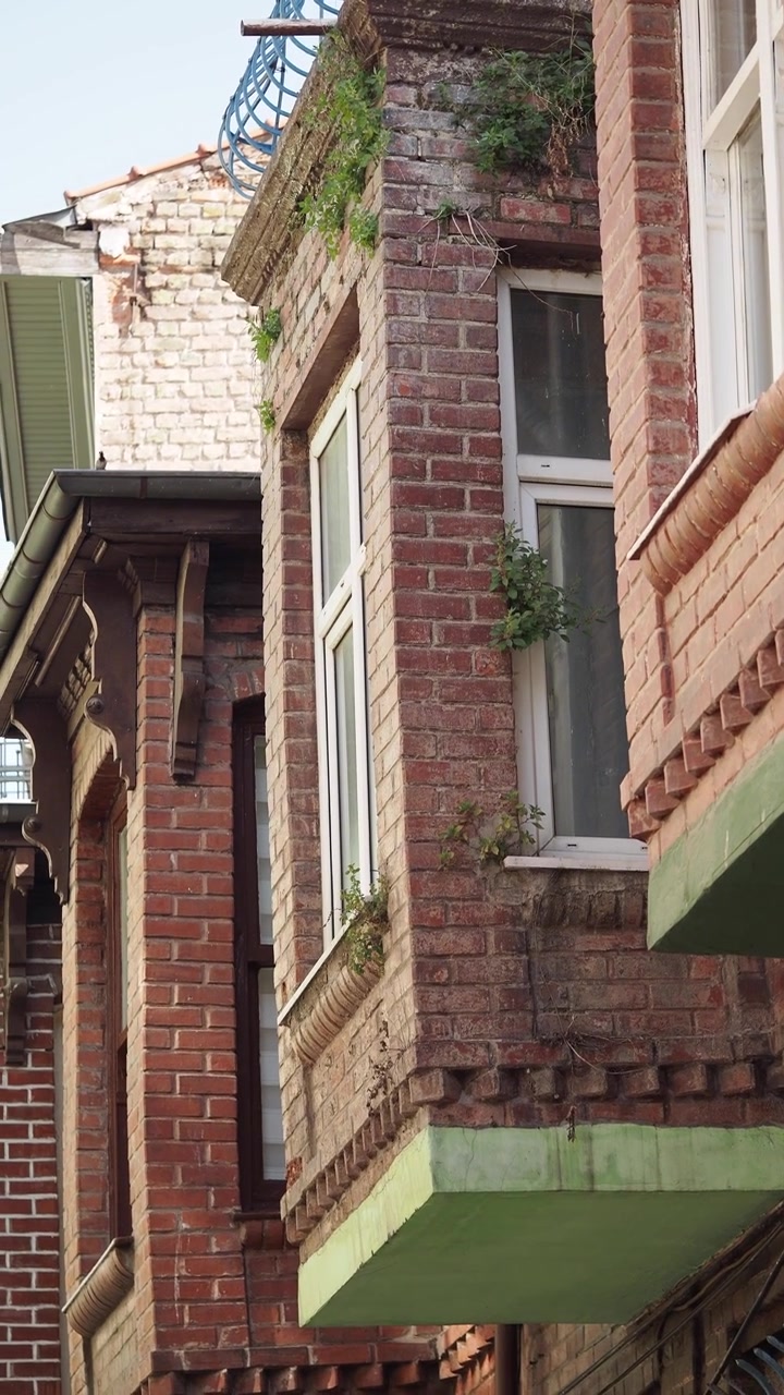 Historische Fassade aus rotem Backstein mit Erkerfenstern und Begrünung.