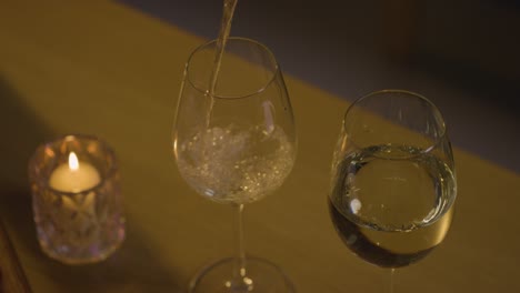 close up of pouring wine into glasses for romantic evening at home in lounge with candles