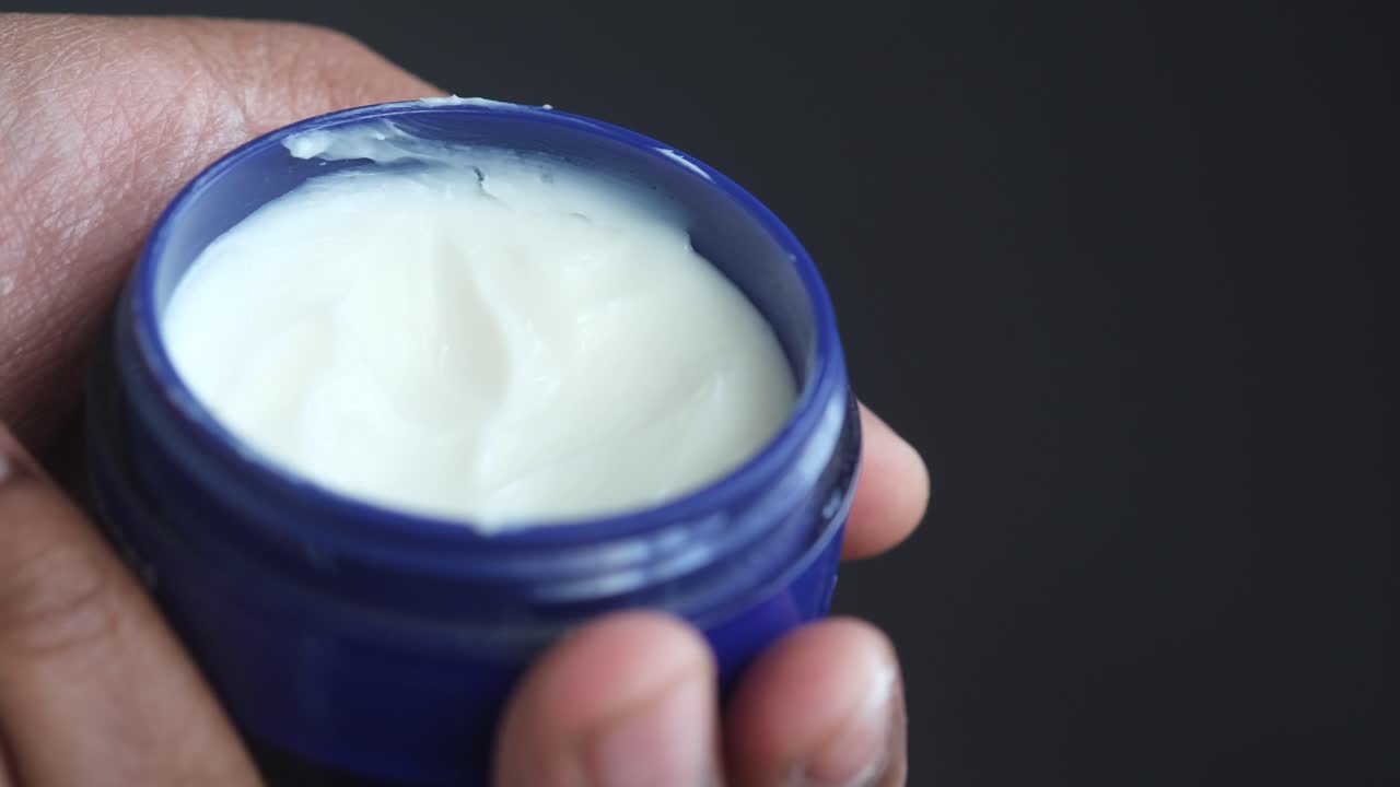 mano sosteniendo un recipiente de crema blanca