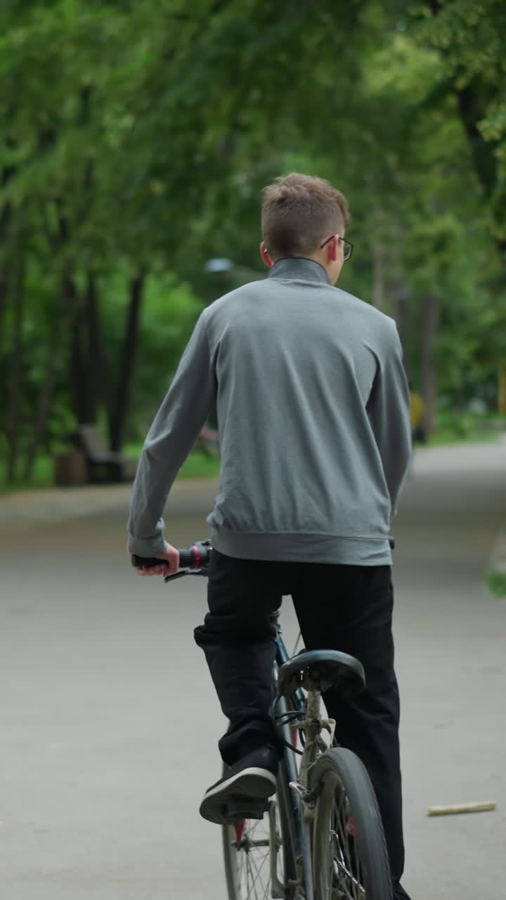 두 친구가 공원 길에서 자전거를 타고 회색 을 입은 사람이 머리를 고, 푸른 나무로 둘러싸인 앞을 고 있는 사람들의 흐릿한 시야와 함께