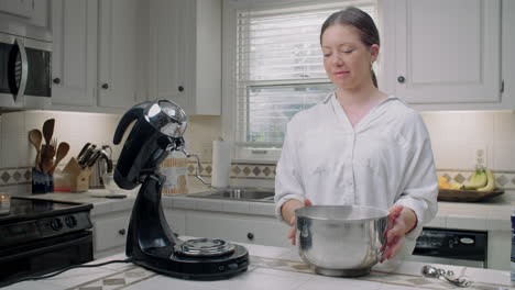 woman in a white shirt puts a bowl onto an electric mixer in her kitchen