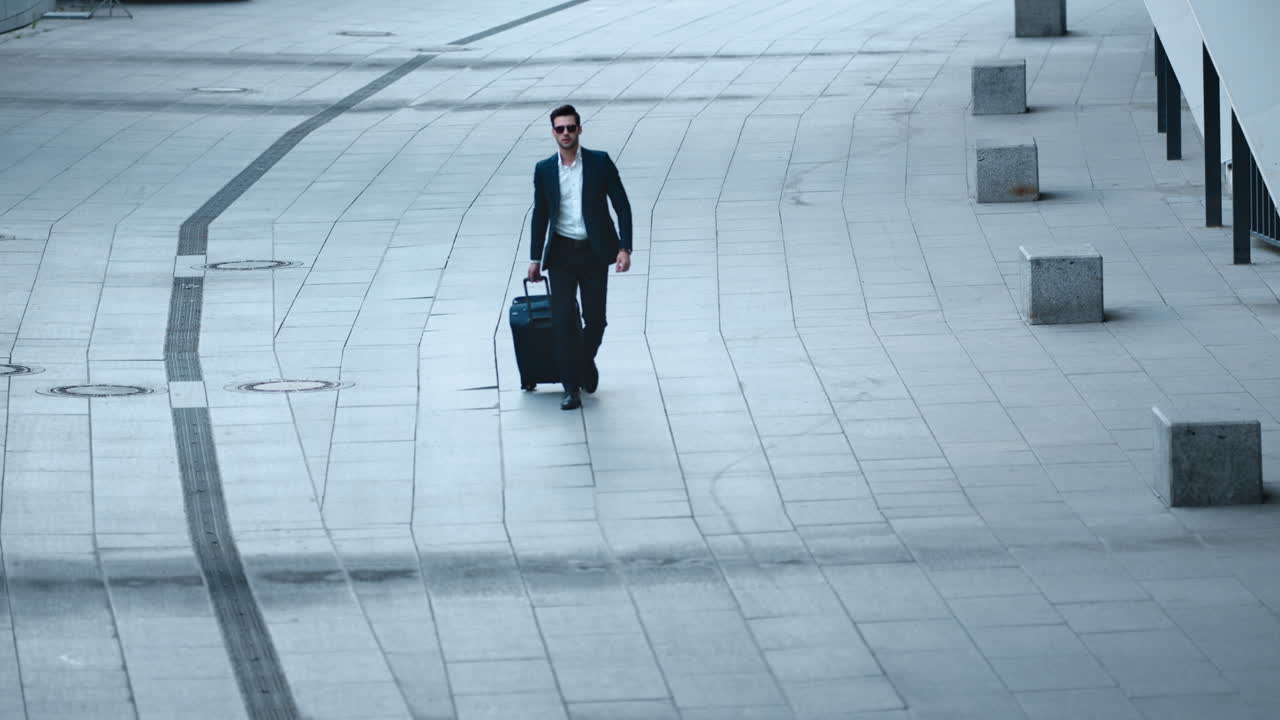 Close up view of handsome businessman walking with luggage on sidewalk