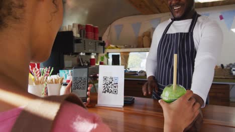 mujer afroamericana haciendo el pago desde su teléfono inteligente escaneando el código qr en el camión de comida