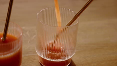 a orange cold pressed juice detox cleanse getting poured in a drinking glass with a metal straw in slow motion