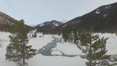 flying over winding river in snow covered rocky mountain valley